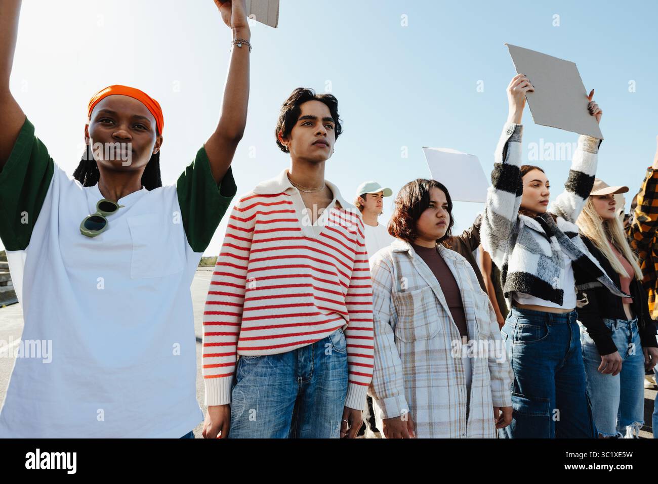 Un gruppo eterogeneo di giovani individui in piedi insieme, tenendo con fiducia dei segni, rappresentando l'unità e l'attivismo durante una protesta all'aperto sotto cle Foto Stock