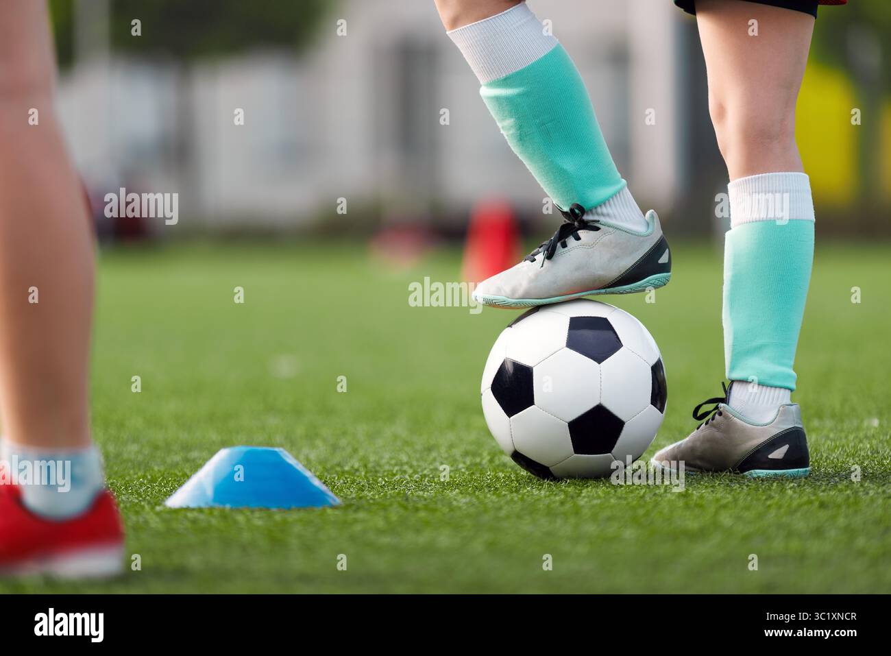 Primo piano di un giovane calciatore con calcio e scarpe da calcio con palla bianca e nera su un campo verde erboso. Calciatori in allenamento Foto Stock Primo piano di un giovane calciatore con calcio e scarpe da calcio con palla bianca e nera su un campo verde erboso. Calciatori in allenamento Foto Stock