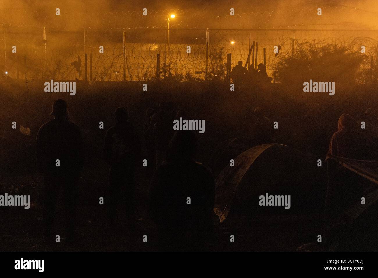 I migranti hanno silhouette vicino alle tende di notte, con recinzioni illuminate e figure di pattugliamento a Ciudad Juarez. Foto Stock