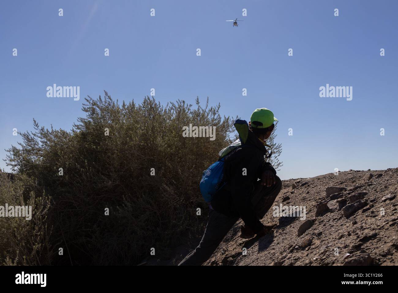 Il migrante con casco verde osserva il pattugliamento in elicottero nel deserto di Ciudad Juarez. Foto Stock