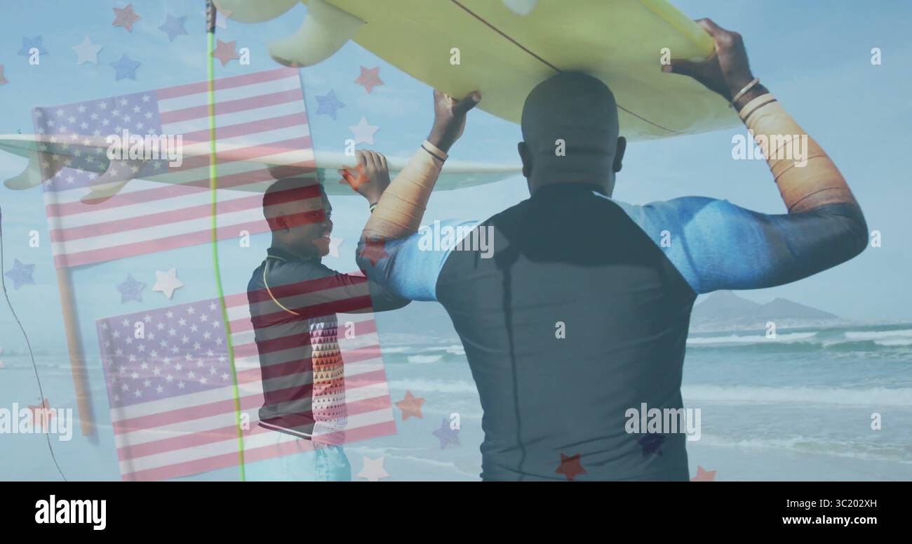 Padre e figlio che camminano indossando muta e trasportando tavole da surf sulla spiaggia sabbiosa, con copertura bandiera Foto Stock