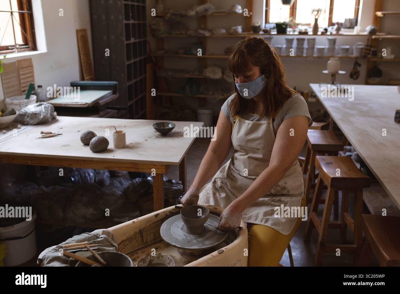 vasaio femminile che forma una ciotola di argilla bagnata sulla ruota rotante in un laboratorio di ceramica, con utensili sui tavoli Foto Stock