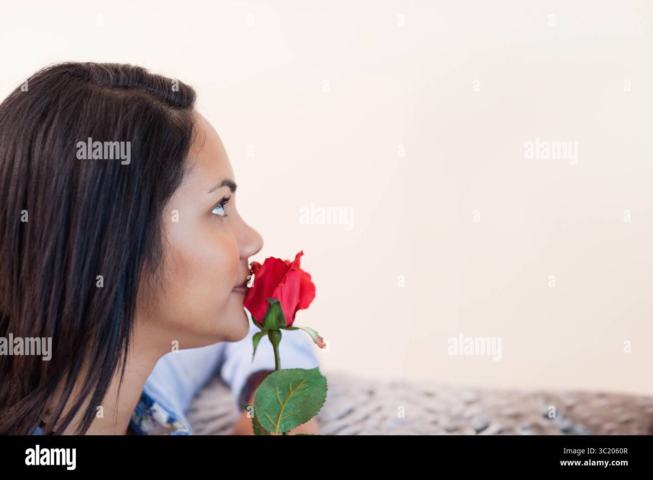 Donna che profuma di rosa rossa mentre siede su un divano a motivi geometrici nell'area soggiorno e nello spazio fotocopie Foto Stock