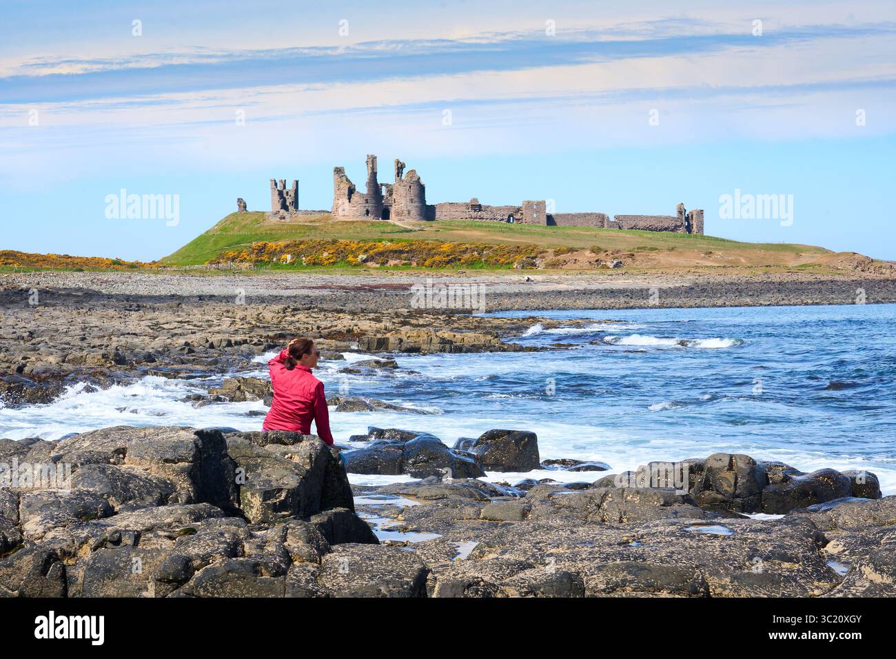 Donna che ammira le rovine medievali del castello di Dunstanburgh nel nord-est dell'Inghilterra, Regno Unito Foto Stock