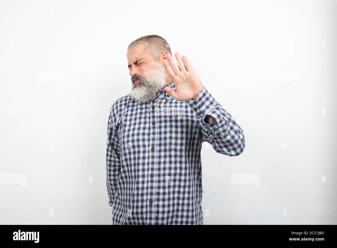 Uomo maturo con capelli grigi e barba che mostra disgusto e fa un gesto di arresto con la mano su sfondo bianco Foto Stock