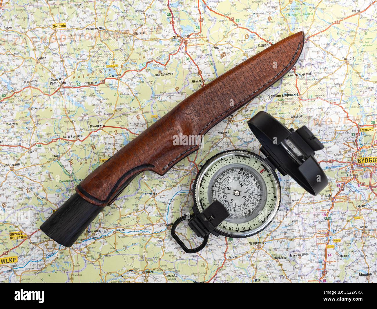 Equipaggiamento da esplorazione all'aperto con una mappa, una bussola e un coltello con una guaina in pelle che simboleggia la navigazione, il viaggio e la preparazione alla natura e. Foto Stock
