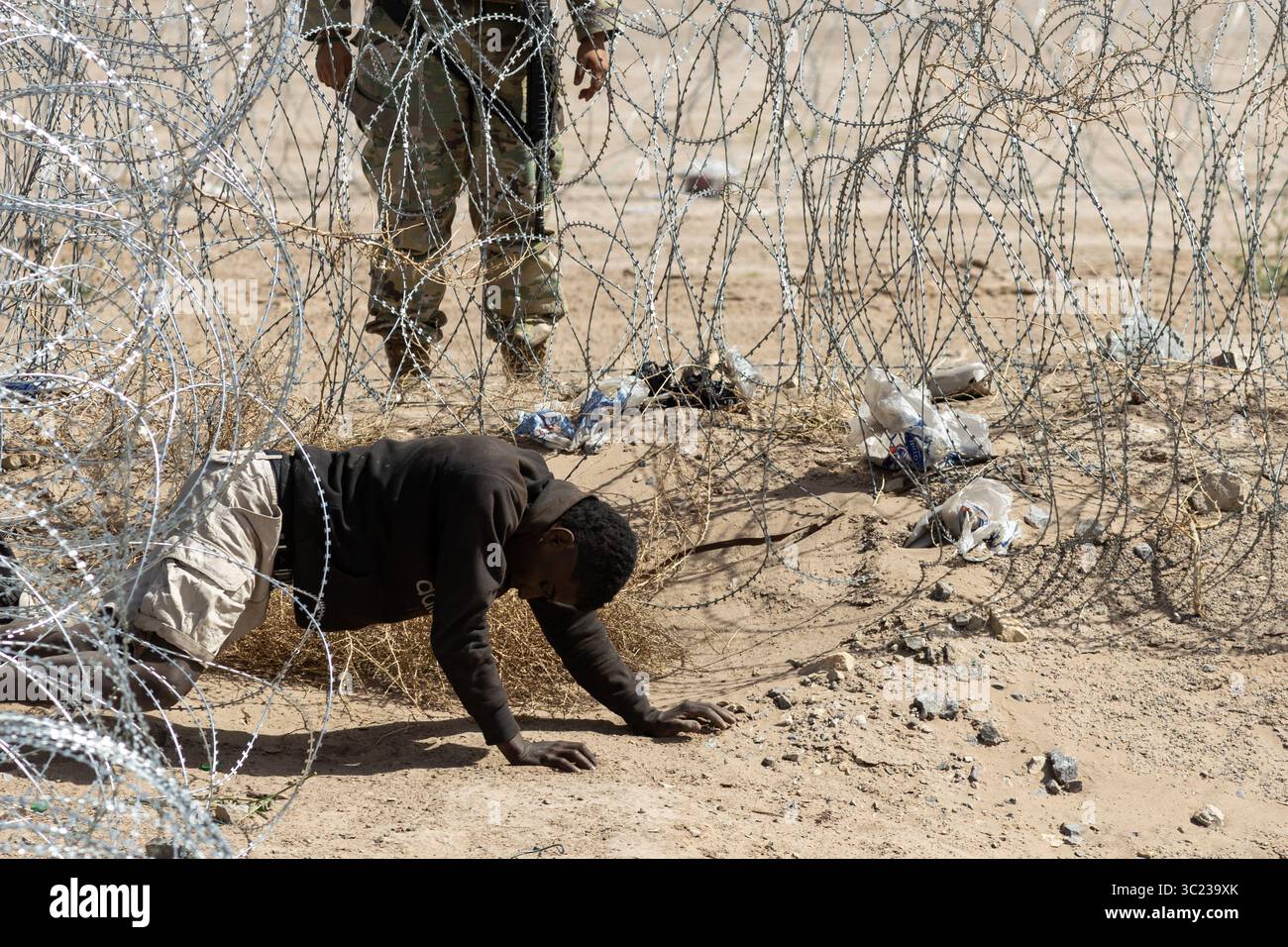 Un migrante braves spinato a Ciudad Juarez, sotto l'occhio vigile di una guardia. Foto Stock