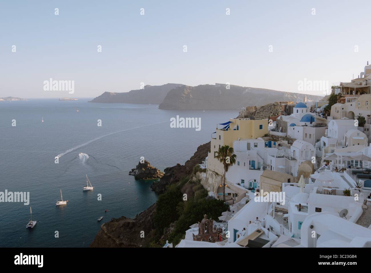 Vista del villaggio di Oia a Santorini, in Grecia, con case cicladiche dipinte di bianco e chiese dalla cupola blu arroccate su una scogliera al tramonto. Foto Stock