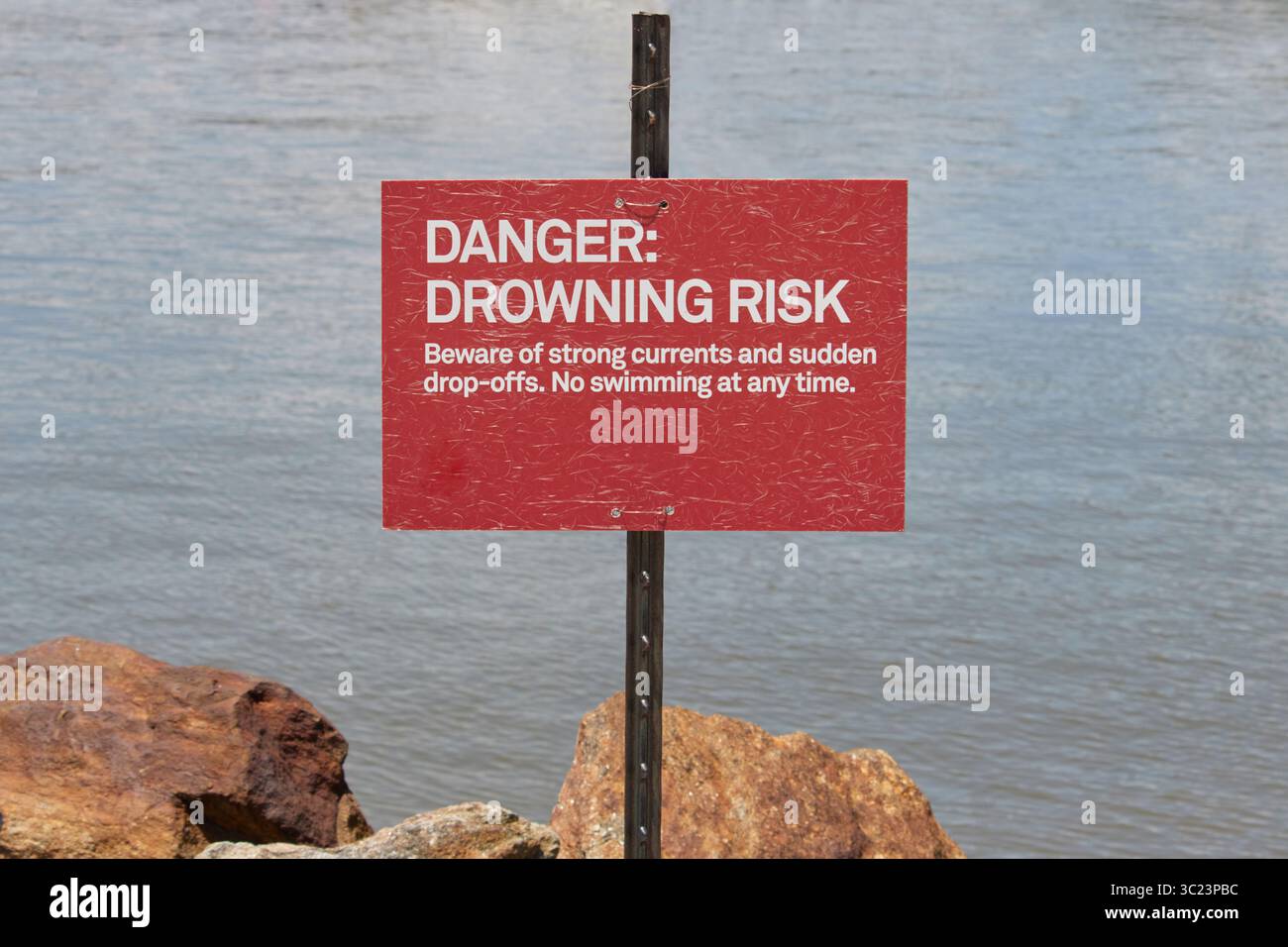 segnale di avvertimento rosso con pericolo, rischio di annegamento, attenzione a forti correnti e cadute improvvise. Non è possibile nuotare in qualsiasi momento. Su un corpo roccioso d'acqua, copia spazio Foto Stock