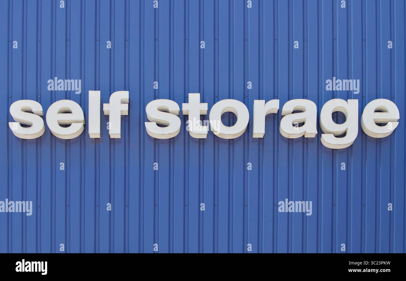 un cartello autoportante con tre lettere bianche di dimensioni su una parete blu in metallo ondulato con spazio di copia Foto Stock