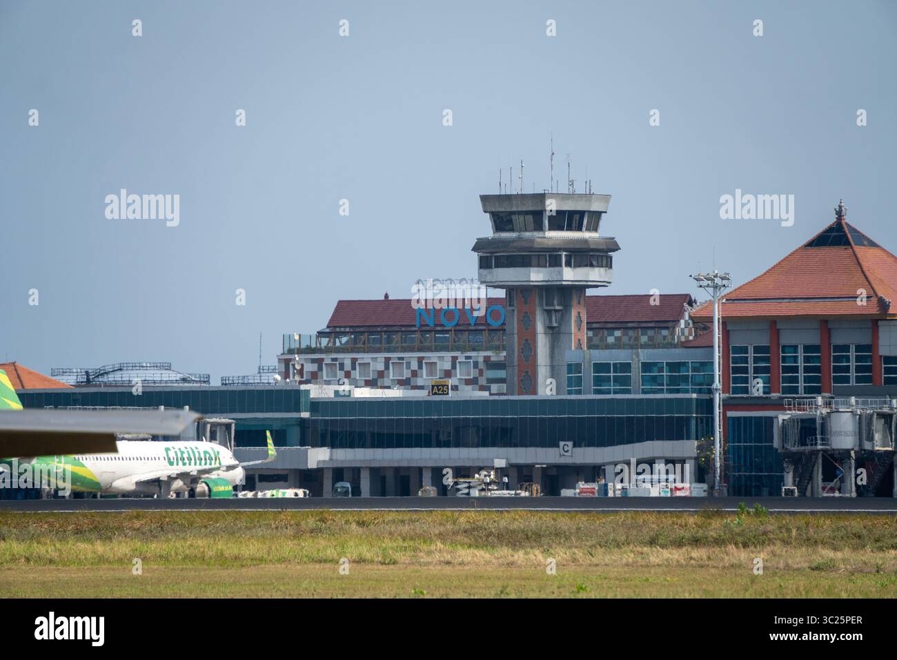 Bali, 18 settembre 2024: Vista della torre di controllo e del terminal dell'aeroporto Ngurah Rai, con la segnaletica Novotel e un aereo Citilink vicino al gate A26. Foto Stock