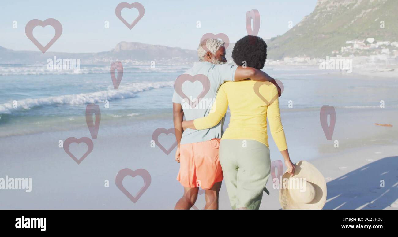Walking Black Couple braccio in braccio lungo la spiaggia sabbiosa, con cappello di paglia a tegole larghe Foto Stock