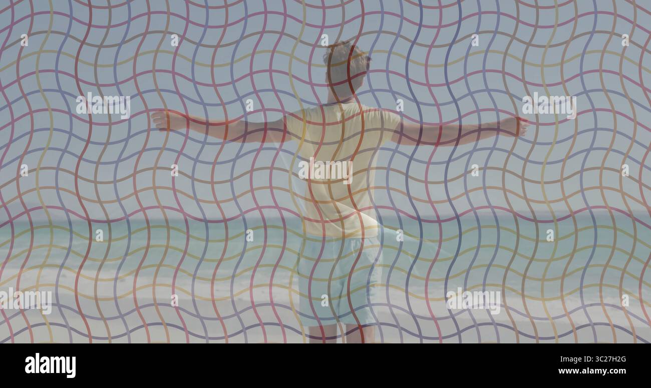 Uomo in equilibrio con pantaloncini da nuoto azzurri che allungano le braccia sulla costa sabbiosa, con onde da surf spumeggianti Foto Stock