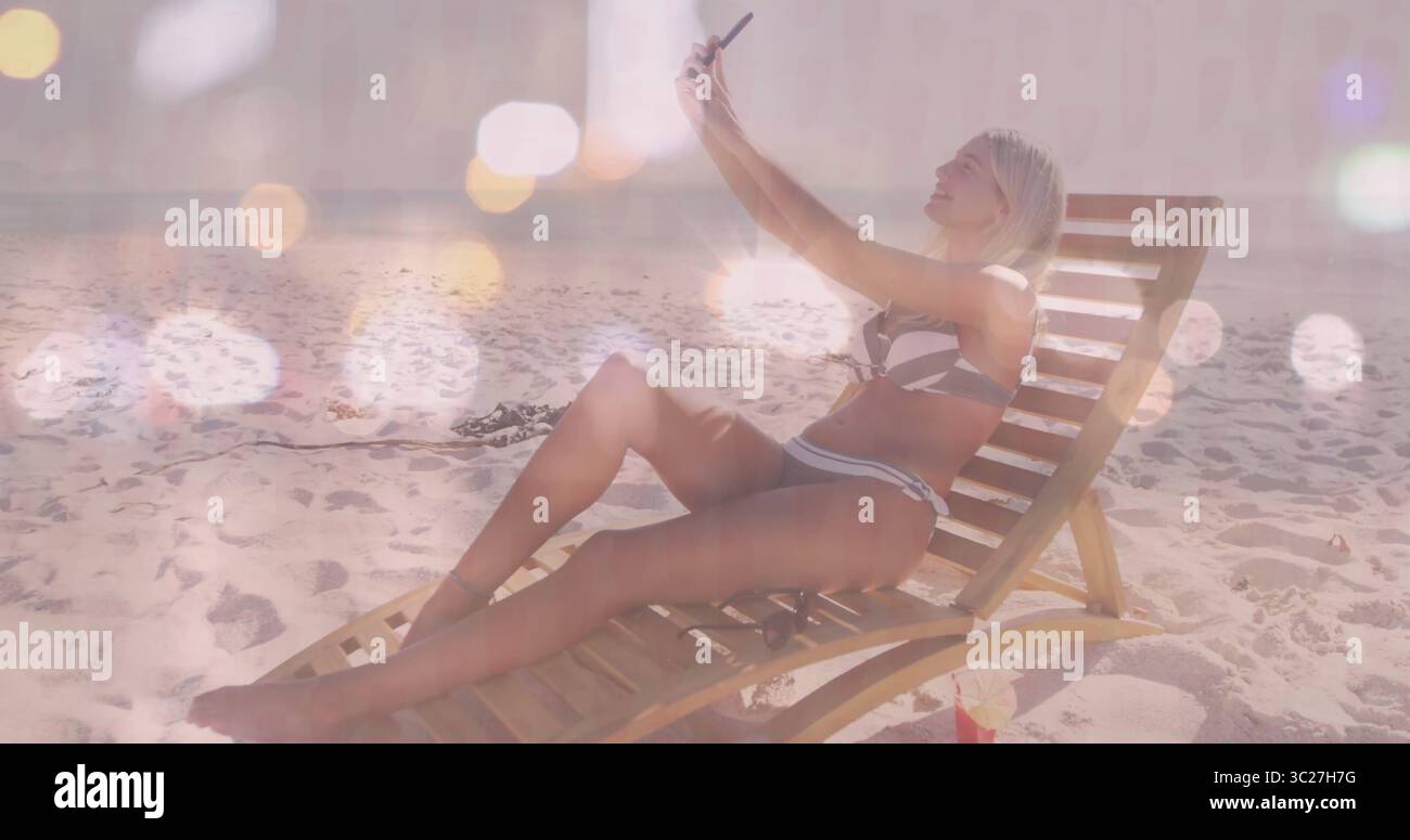 In mano smartphone, donna in costume da bagno a righe sdraiata sulla sdraio in spiaggia, con borsa rossa Foto Stock