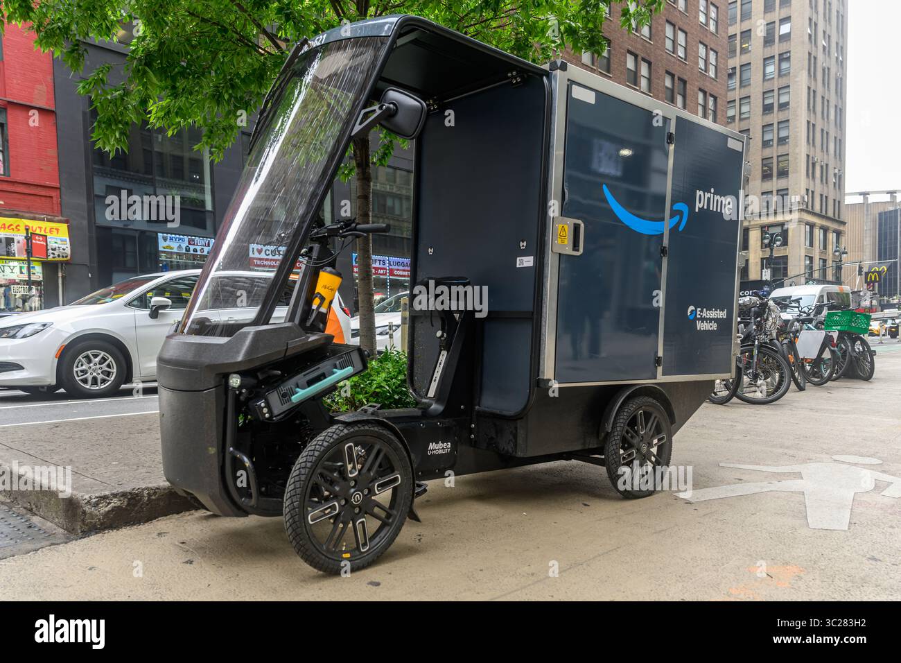 Una eCargobike Amazon Mubea parcheggiata sulla 8th Ave, New York City, USA, mentre il subacqueo effettua Una consegna a casa. Foto Stock