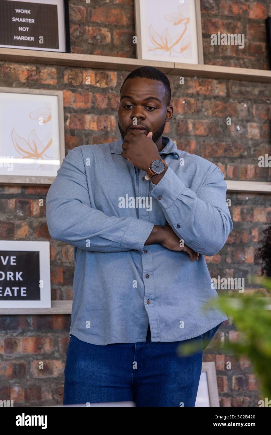 Uomo afro-americano in piedi con cura negli uffici con scaffali in legno e cartelli motivazionali Foto Stock