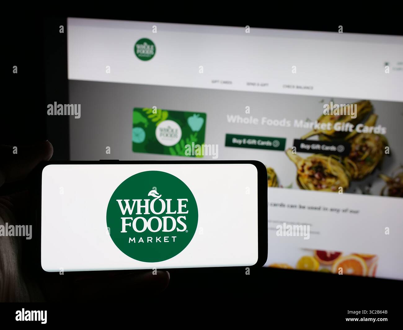 Stoccarda, Germania - 05-25-2025: Persona che possiede uno smartphone con il logo della società statunitense di vendita al dettaglio Whole Foods Market Inc. Sullo schermo davanti al sito Web. Foto Stock Stoccarda, Germania - 05-25-2025: Persona che possiede uno smartphone con il logo della società statunitense di vendita al dettaglio Whole Foods Market Inc. Sullo schermo davanti al sito Web. Foto Stock