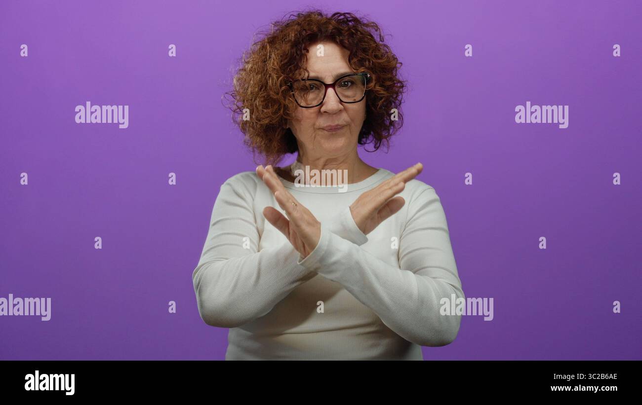 La donna ispanica di mezza età si ferma in una parte superiore bianca su uno sfondo viola isolato. Foto Stock