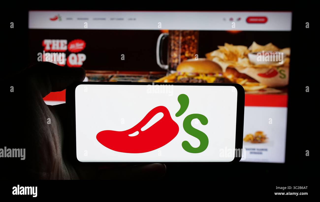 Stoccarda, Germania - 05-25-2025: Persona che tiene il cellulare con il logo della catena di ristoranti americana Chilis Grill Bar sullo schermo davanti alla pagina web. Foto Stock