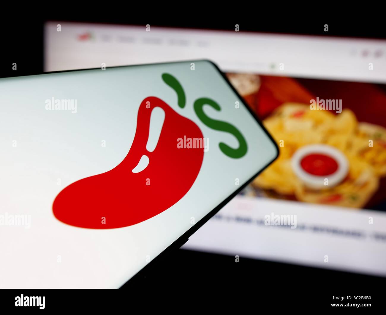 Stoccarda, Germania - 05-25-2025: Smartphone con logo della catena di ristoranti americana Chili's Grill Bar sullo schermo davanti al sito Web. Foto Stock
