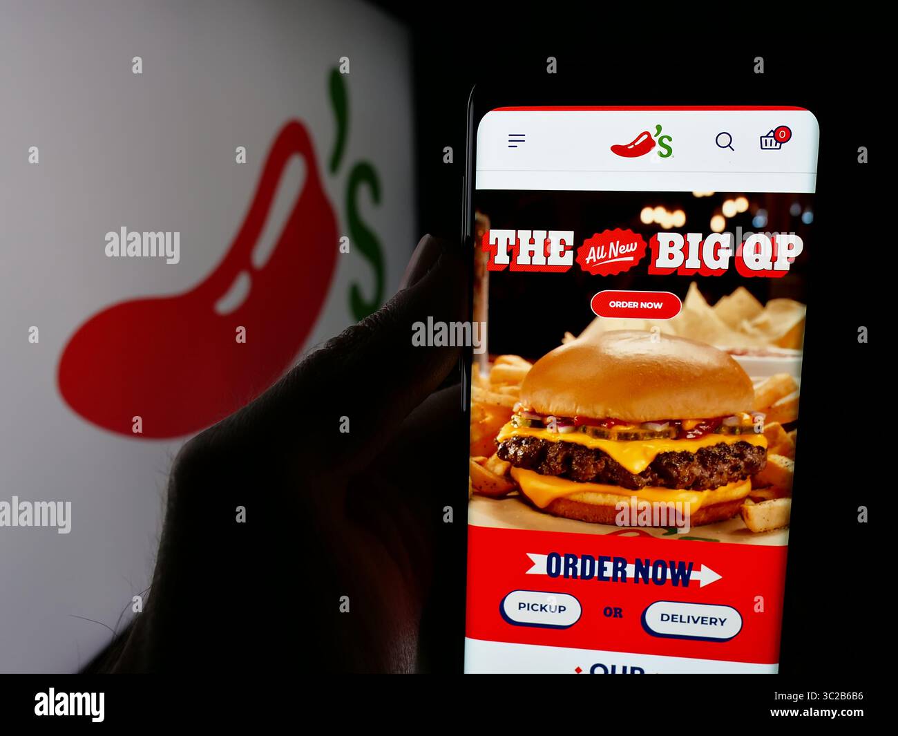 Stoccarda, Germania - 05-25-2025: Persona che tiene in mano lo smartphone con la pagina web della catena di ristoranti americana Chili's Grill Bar sullo schermo davanti al logo. Foto Stock