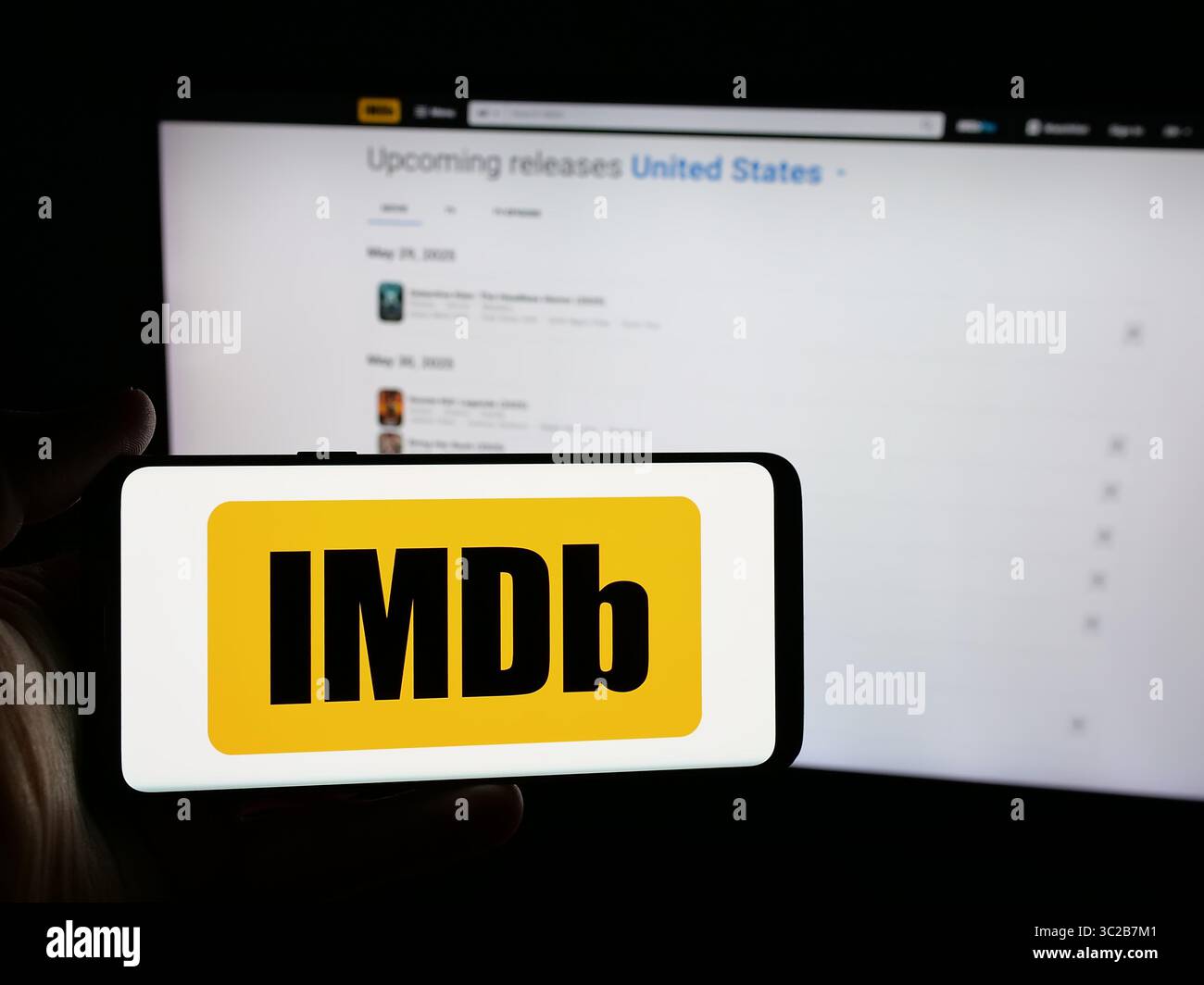 Stoccarda, Germania - 05-27-2025: Persona che possiede uno smartphone con logo della piattaforma statunitense Internet Movie database (IMDb) sullo schermo davanti al sito web. Foto Stock