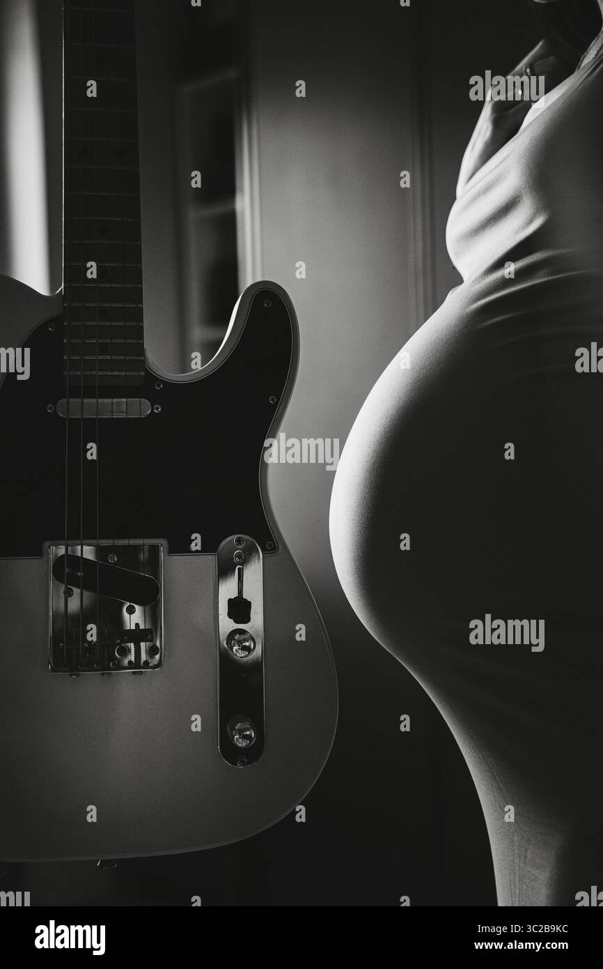 Foto in bianco e nero con una donna incinta accanto a una chitarra, evidenziando il legame tra musica e maternità. La scena trasmette un sereno e Foto Stock