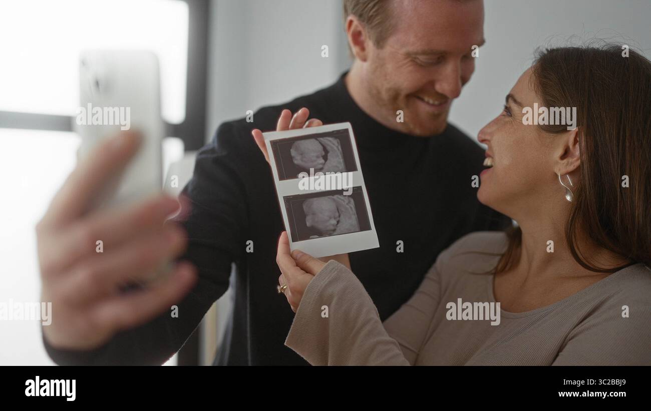 Accoppiatevi con gioia scattando selfie con immagini a ultrasuoni in un ambiente accogliente, evidenziando l'emozione e l'anticipazione del viaggio di gravidanza insieme. Foto Stock
