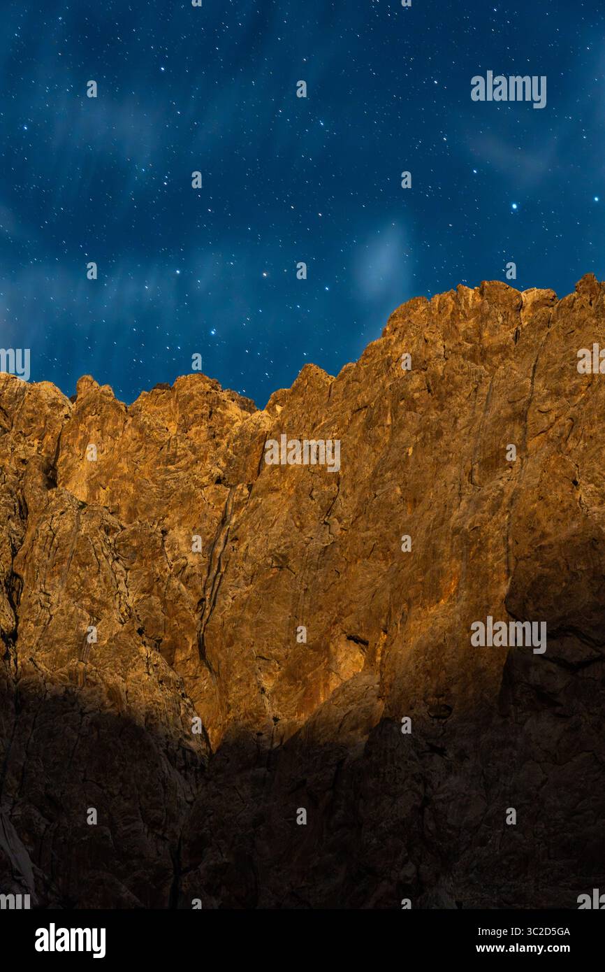 Una vista mozzafiato di un cielo stellato e limpido sopra un'aspra parete di montagna illuminata, che mostra la bellezza celeste Foto Stock
