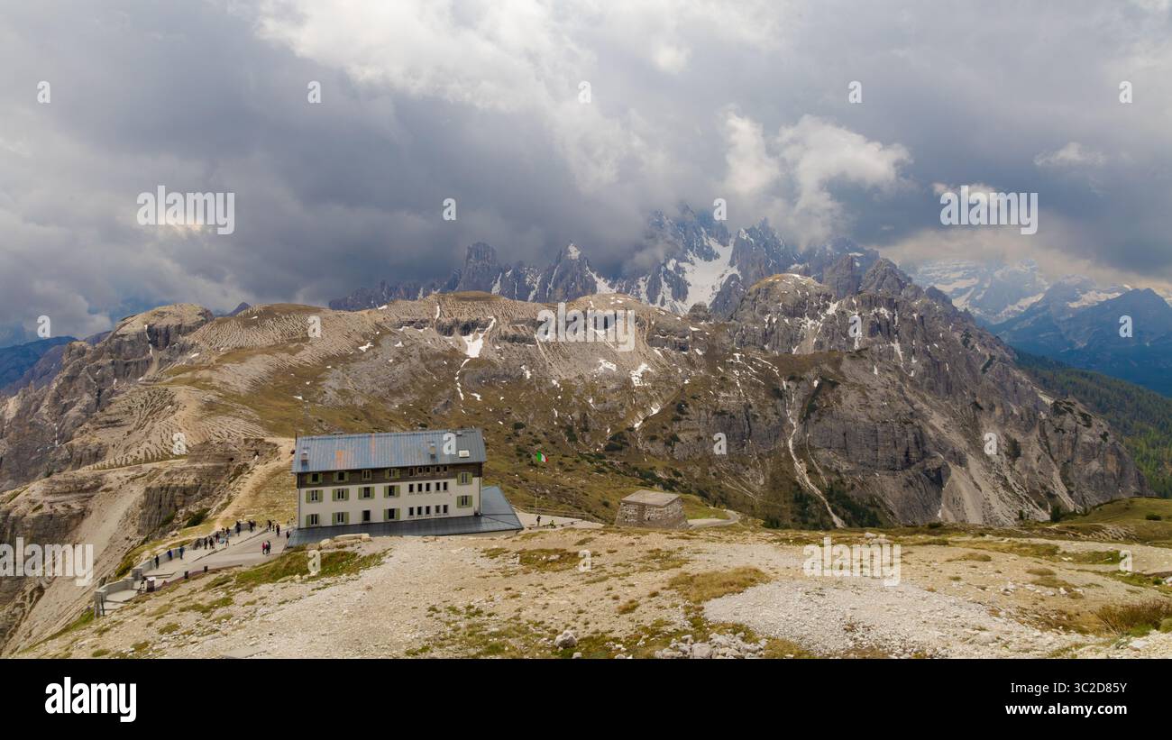 Rifugio di montagna alle tre Cime di Lavaredo con cime rocciose spettacolari, cieli nuvolosi e macchie di neve sparse nelle Dolomiti. Foto Stock