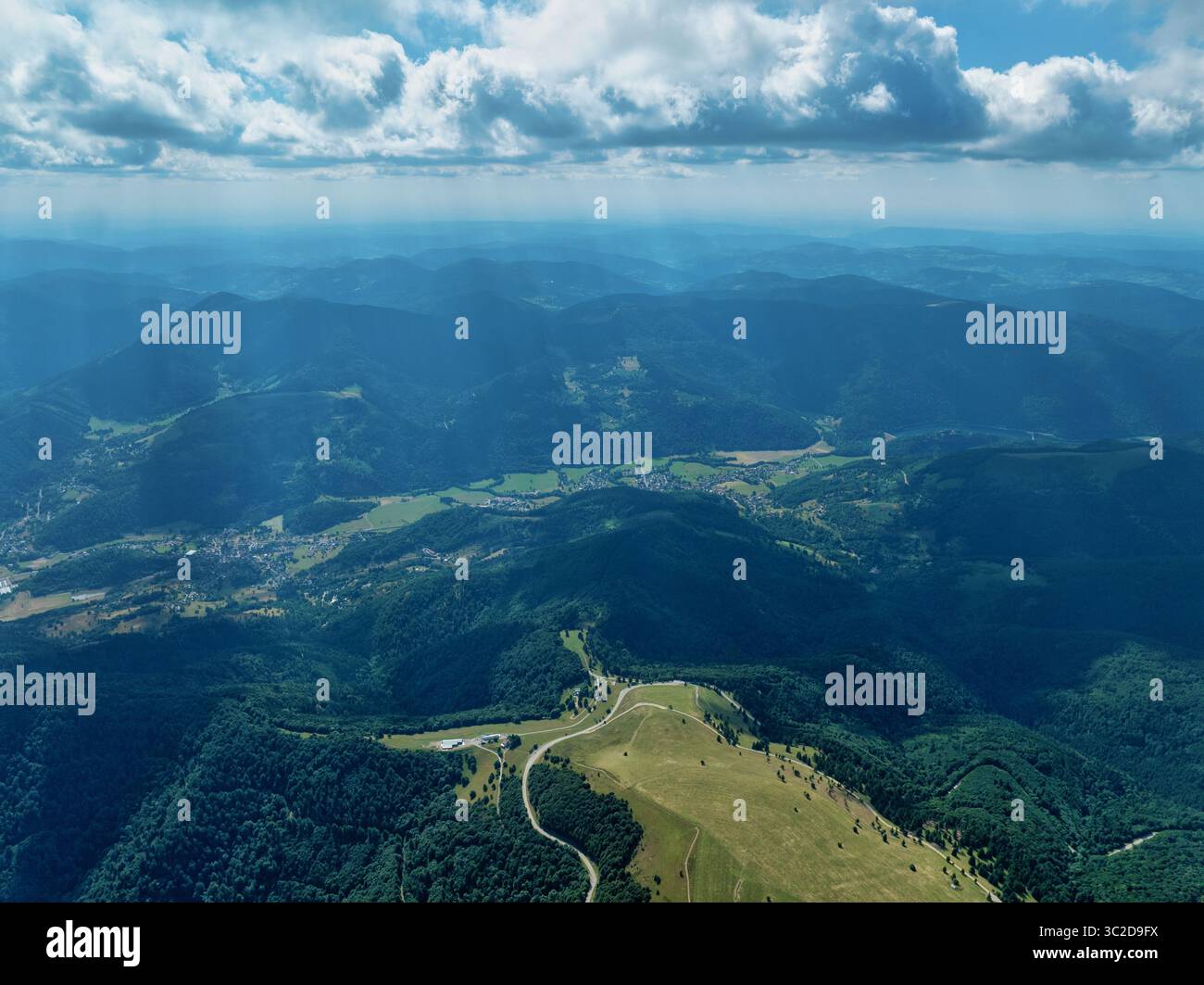 Vista aerea di colline ondulate e valli ricoperte di fitte foreste, intervallate da sacche di civiltà sotto un cielo di nuvole sparse, Oderen, Grand Est, Francia. Foto Stock