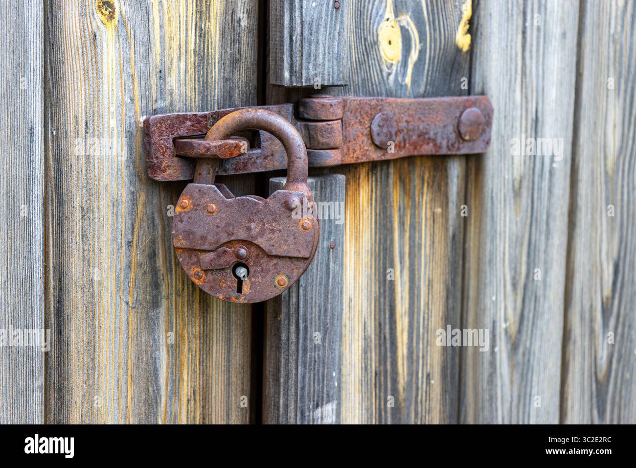Primo piano di un lucchetto arrugginito e antico e di un lucchetto su una porta in legno resistente agli agenti atmosferici, che mostra texture antiche e fascino vintage Foto Stock