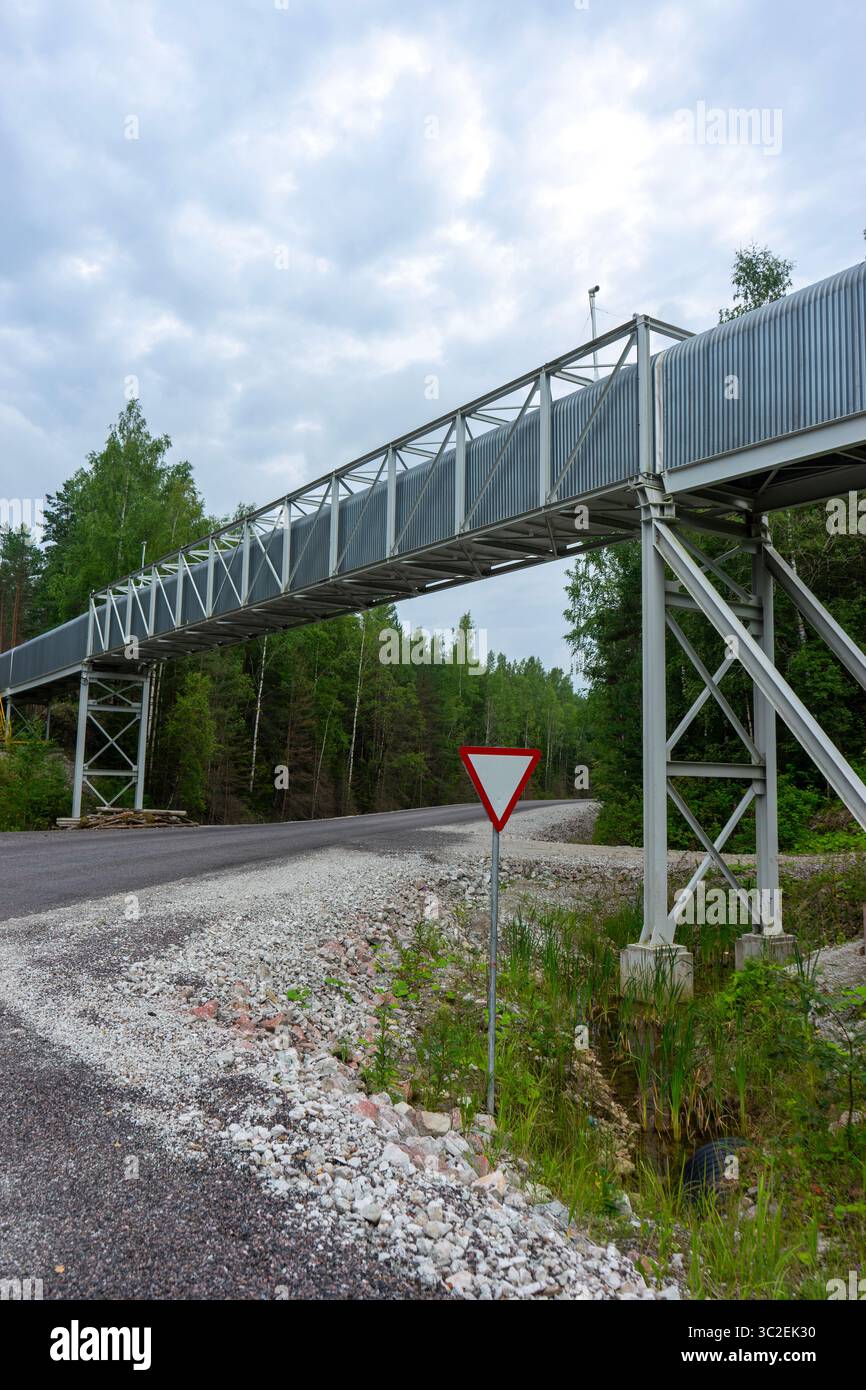 Struttura del nastro trasportatore rialzata in un'area mineraria, che si estende attraverso un paesaggio boschivo Foto Stock