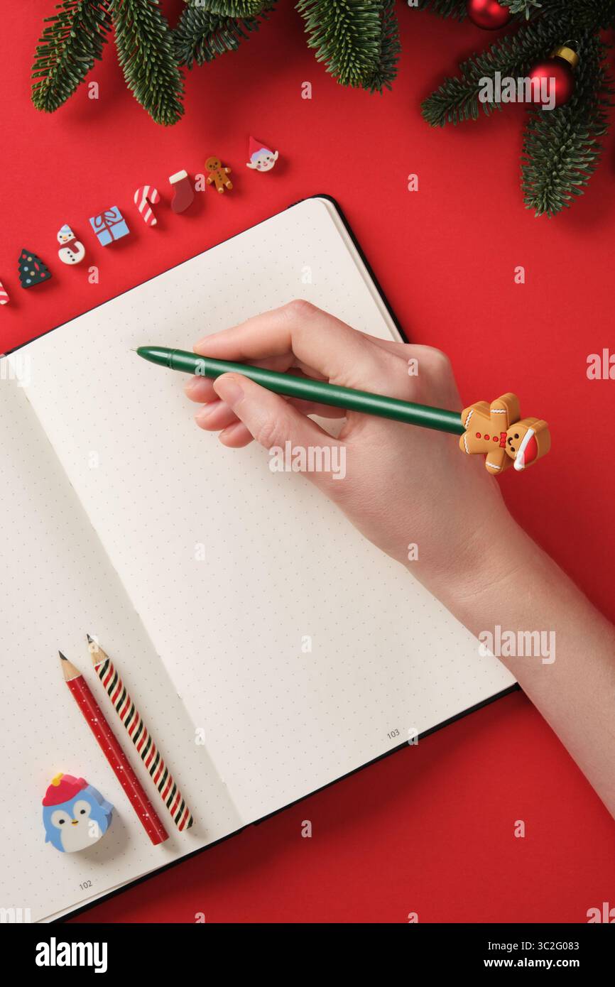 Scrivere a mano i desideri, la lista dei desideri, le promesse o i piani di Capodanno in un quaderno. Sfondo rosso, copia spazio. Foto Stock