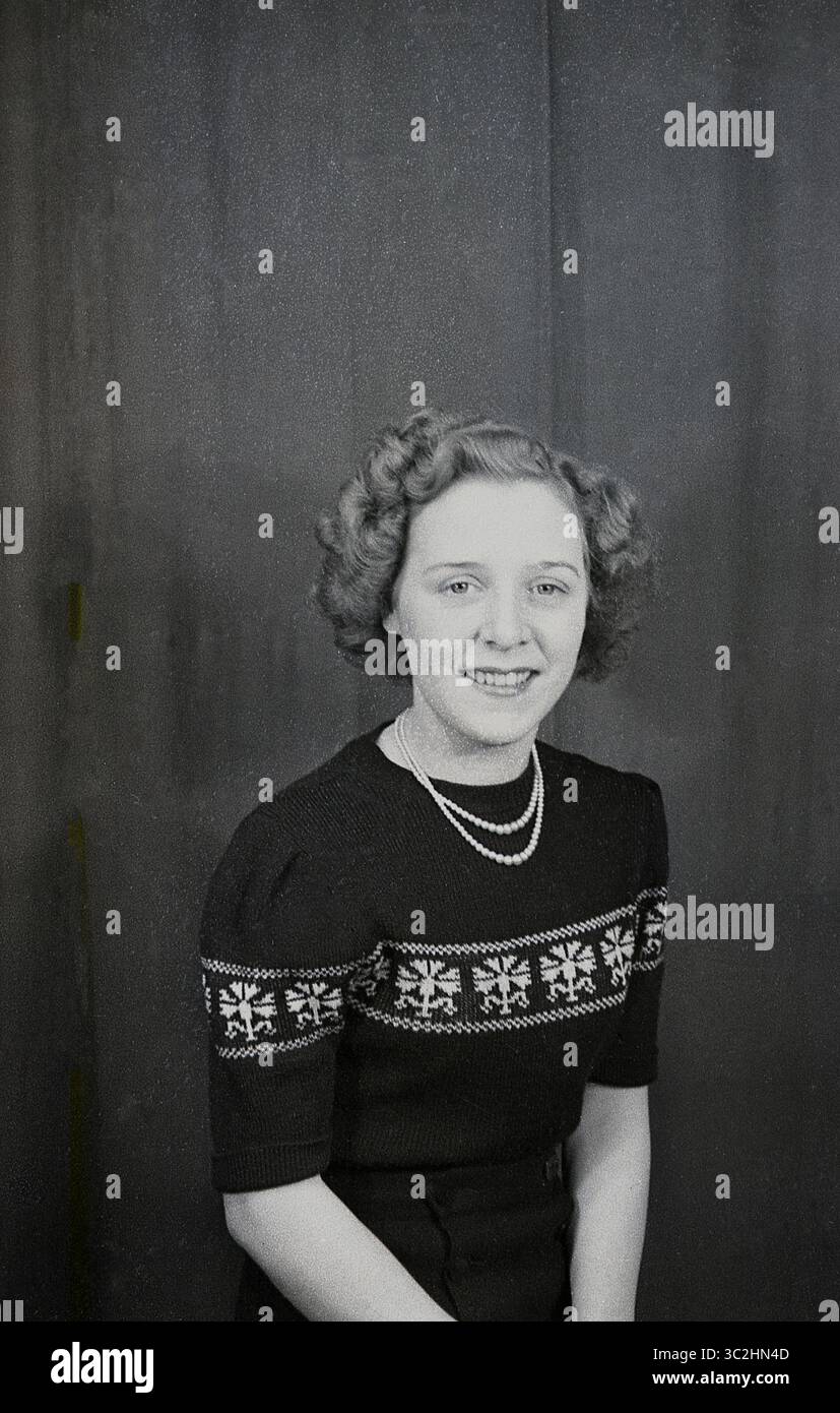 Anni '1950, storica, una bella giovane signora seduta per il suo ritratto in uno studio fotografico, una cosa comune per le persone e le famiglie di quest'epoca da fare, Inghilterra, Regno Unito. Indossa un girocollo, un top in lana a manica corta, ricamato con motivi trasversali e una collana di perle. Foto Stock