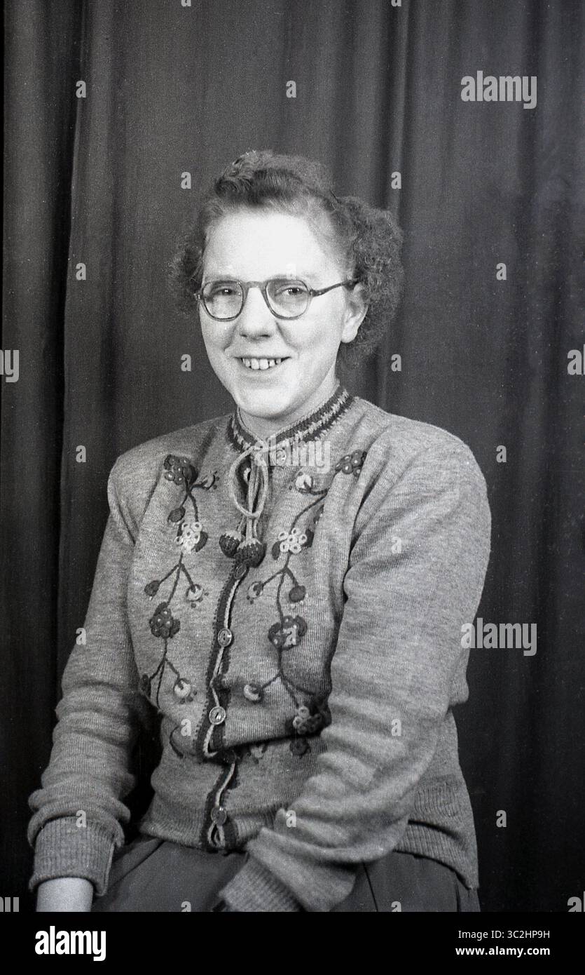 anni '1950, storico, studio fotografico... Una giovane donna seduta per la sua foto, che indossa un cardigan decorato in lana a maniche lunghe, con girocollo, Inghilterra, Regno Unito. Foto Stock