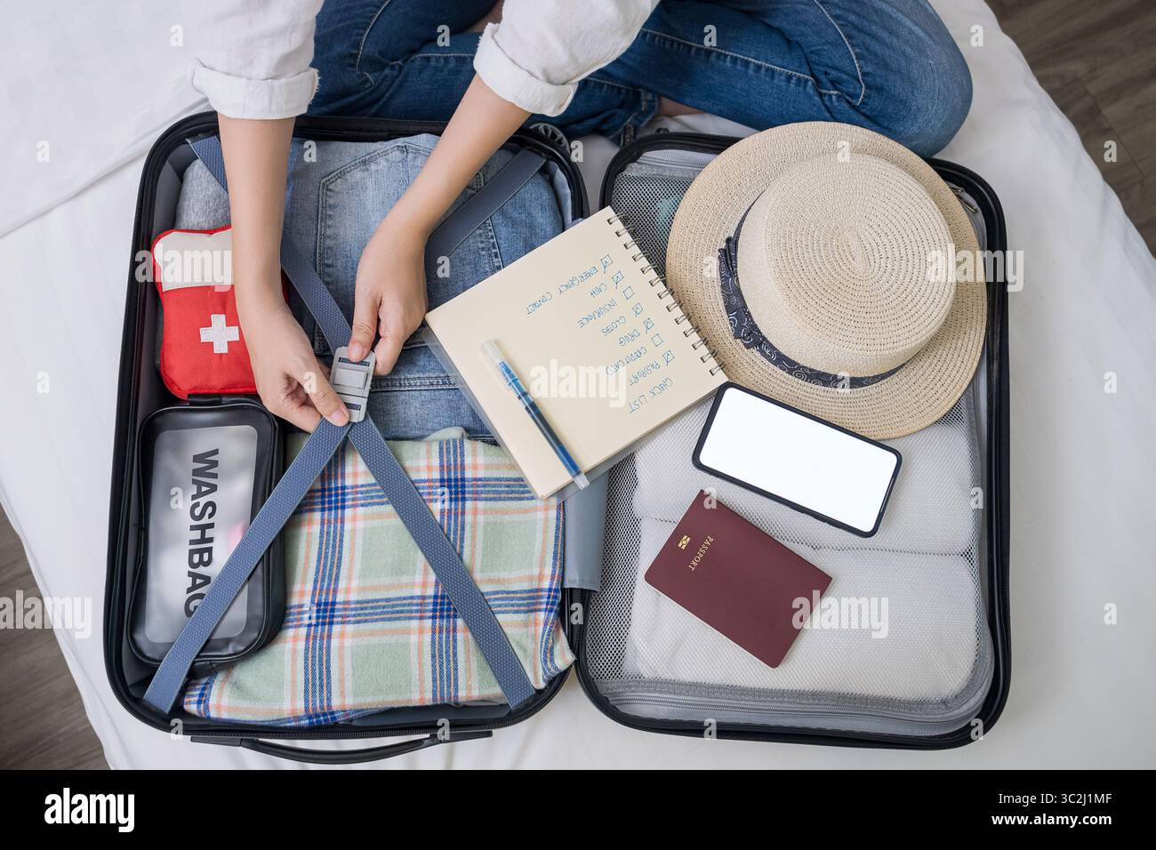 vista dall'alto della donna che sta imballando a mano la valigia per il viaggio, preparandosi per le vacanze estive all'estero con kit di pronto soccorso medico da viaggio, panno, accessorio, telefono moc Foto Stock