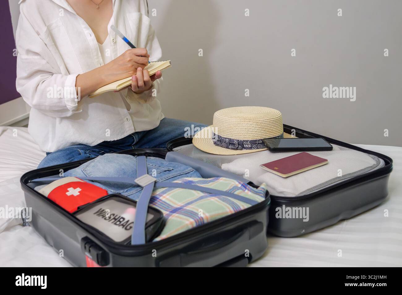 fare una lista di controllo degli oggetti da portare in viaggio. donna che scrive l'articolo della checklist sul notebook e la valigia per andare in vacanza, preparare vestiti, medicine Foto Stock