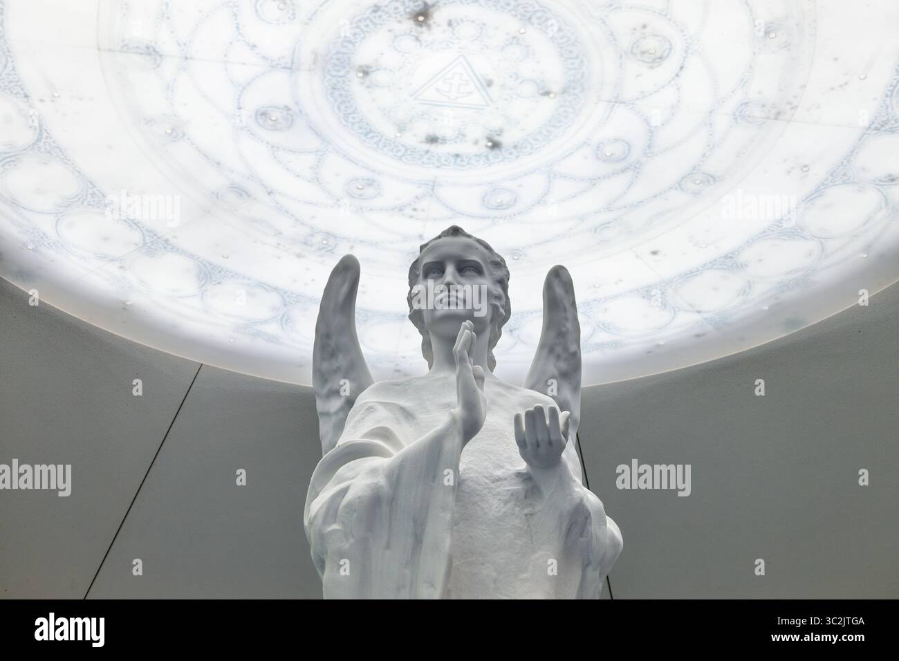 Statua bianca angelica che prega sotto una cupola luminosa ornata in un moderno interno sacro Foto Stock