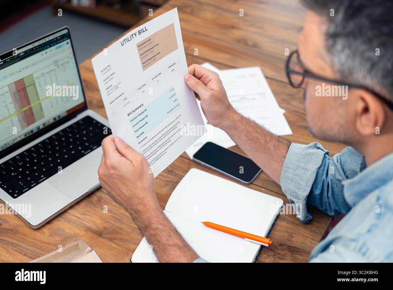 L'inquilino dai capelli grigi tiene a tavola una bolletta stampata con notebook e laptop in crescita Foto Stock