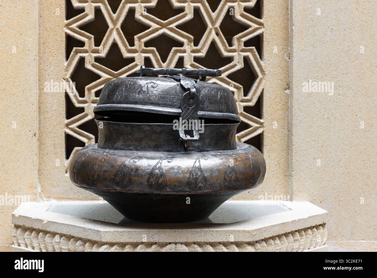 Un'antica portagioie in metallo con manico e intricate incisioni, collocata su uno sfondo geometrico decorativo, che mette in mostra la cura artigianale dei dettagli Foto Stock