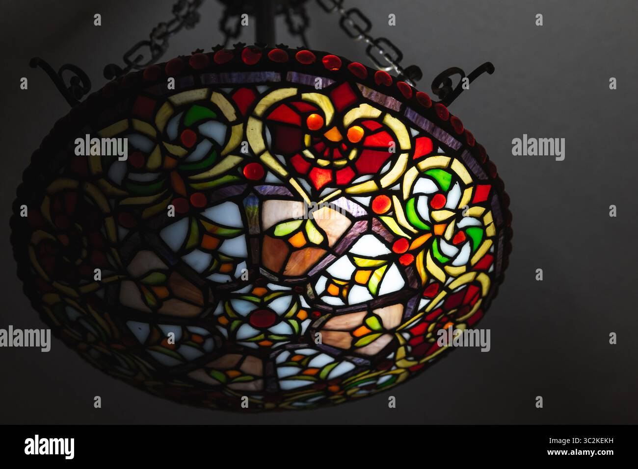 Vivace lampada in vetro colorato con motivi intricati sospesa su sfondo scuro, che enfatizza l'ambiente artistico e artigianale adatto per interni eleganti Foto Stock