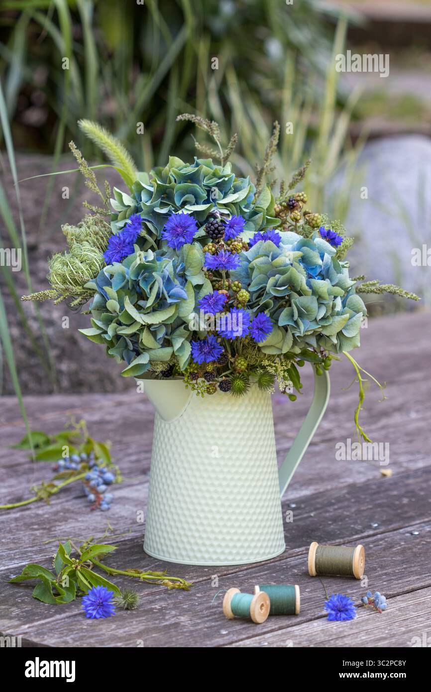 bouquet di ortensie blu in fiore, rosa piuma, rami di mora, carote selvatiche e erbe in una brocca vintage in giardino Foto Stock