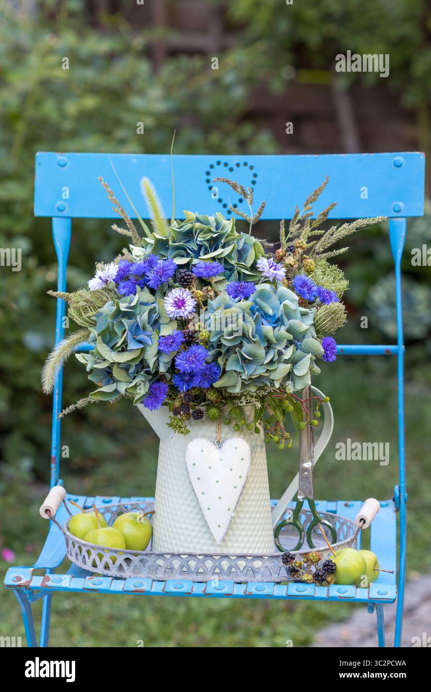 bouquet di ortensie blu in fiore, rosa piuma, rami di mora, carote selvatiche e erbe in una brocca vintage in giardino Foto Stock