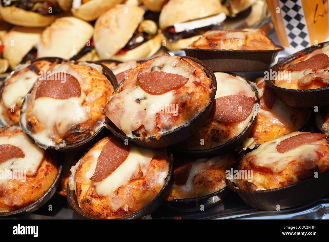 Le mini pizze sono esposte all'aperto in vassoi da forno neri, ricoperte di formaggio fuso e fette di peperoni. La crosta è dorata Foto Stock
