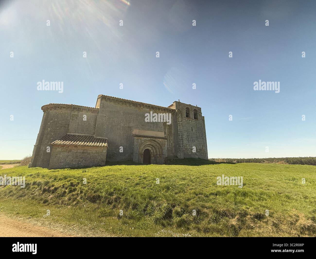 Storica chiesa romanica di San Martino a Matalbaniega, Spagna, con mura in pietra e un campanile sotto un cielo azzurro Foto Stock