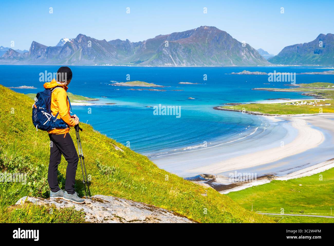 L'escursionista femminile gode di una vista spettacolare sulle montagne e sulla spiaggia di Yttersand da Trail a Roren, Isole Lofoten, Norvegia Foto Stock