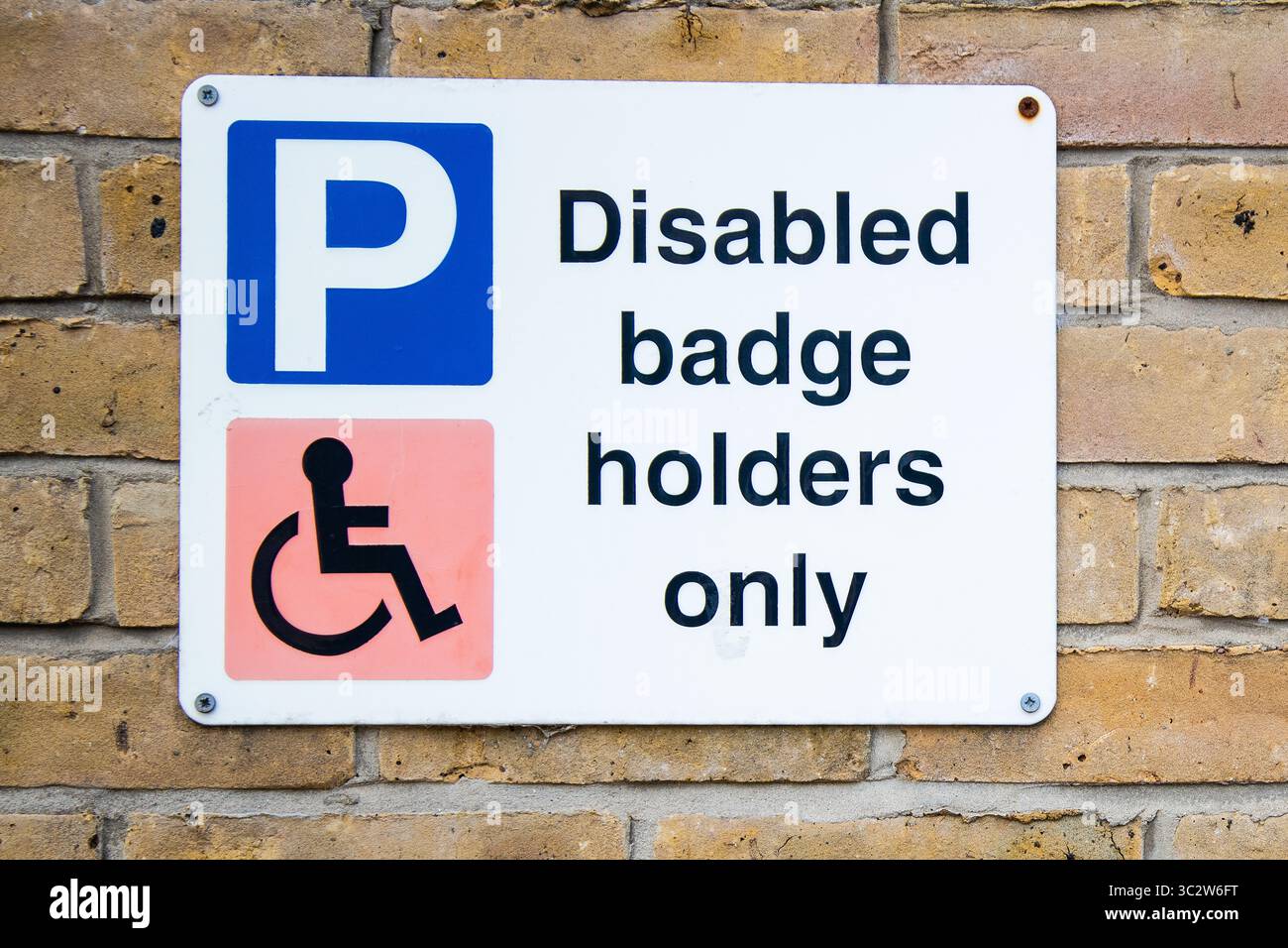 Solo i titolari di badge per disabili sono dotati di segnale di parcheggio montato su una parete in mattoni, che indica il parcheggio limitato per i titolari di badge blu in un'area designata. Foto Stock