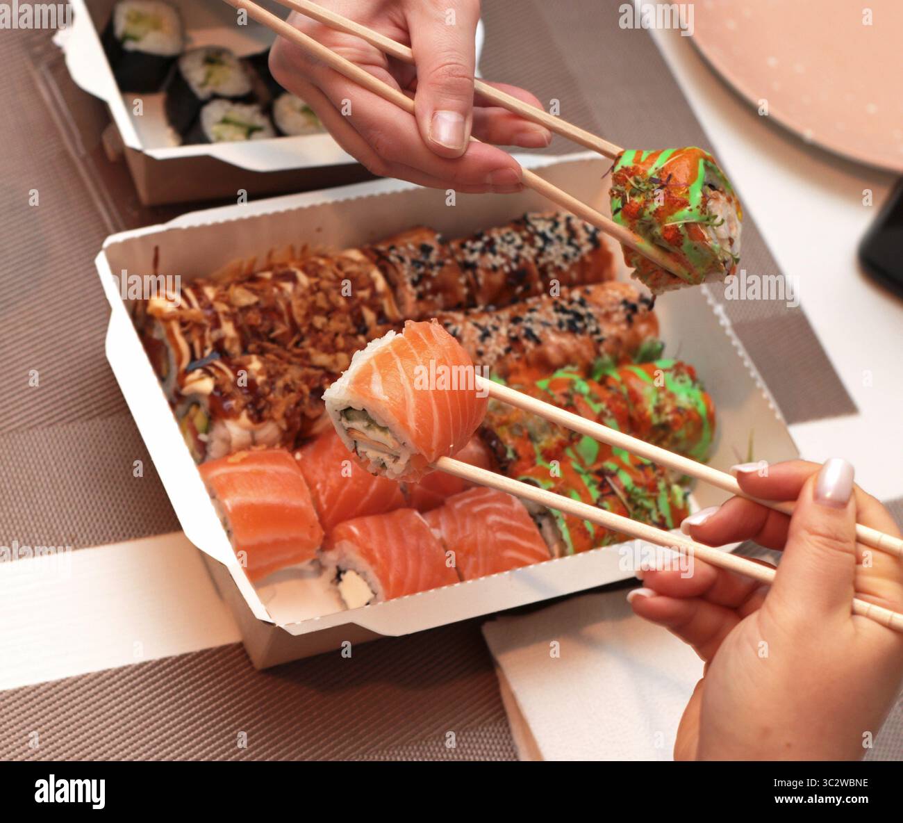 Un invitante shot di sushi roll disposti elegantemente su un tavolo. Mani delicate con bacchette, che mettono in mostra l'arte della cena. Nelle vicinanze, tovaglioli Foto Stock