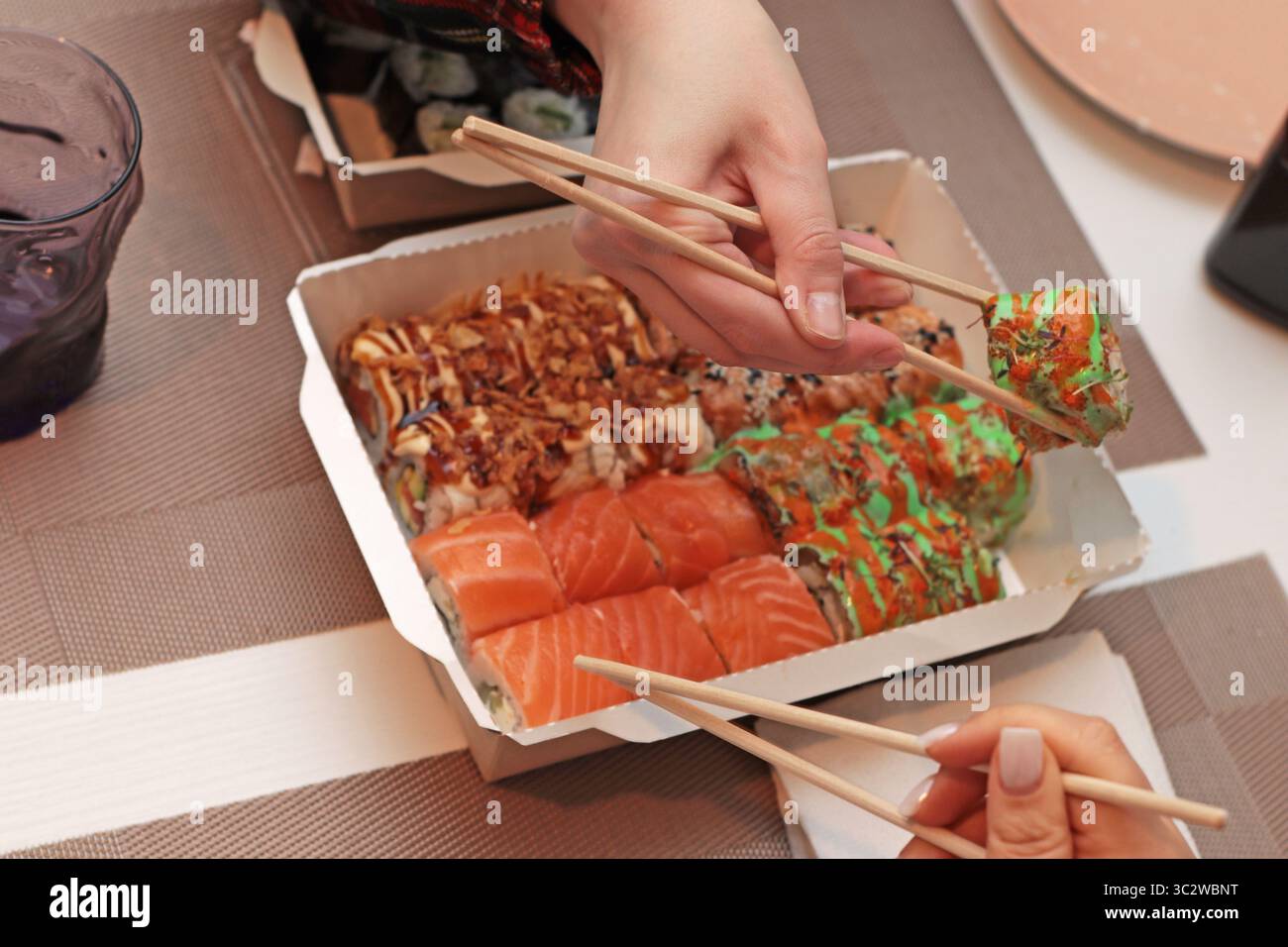 Un invitante shot di sushi roll disposti elegantemente su un tavolo. Mani delicate con bacchette, che mettono in mostra l'arte della cena. Nelle vicinanze, tovaglioli Foto Stock